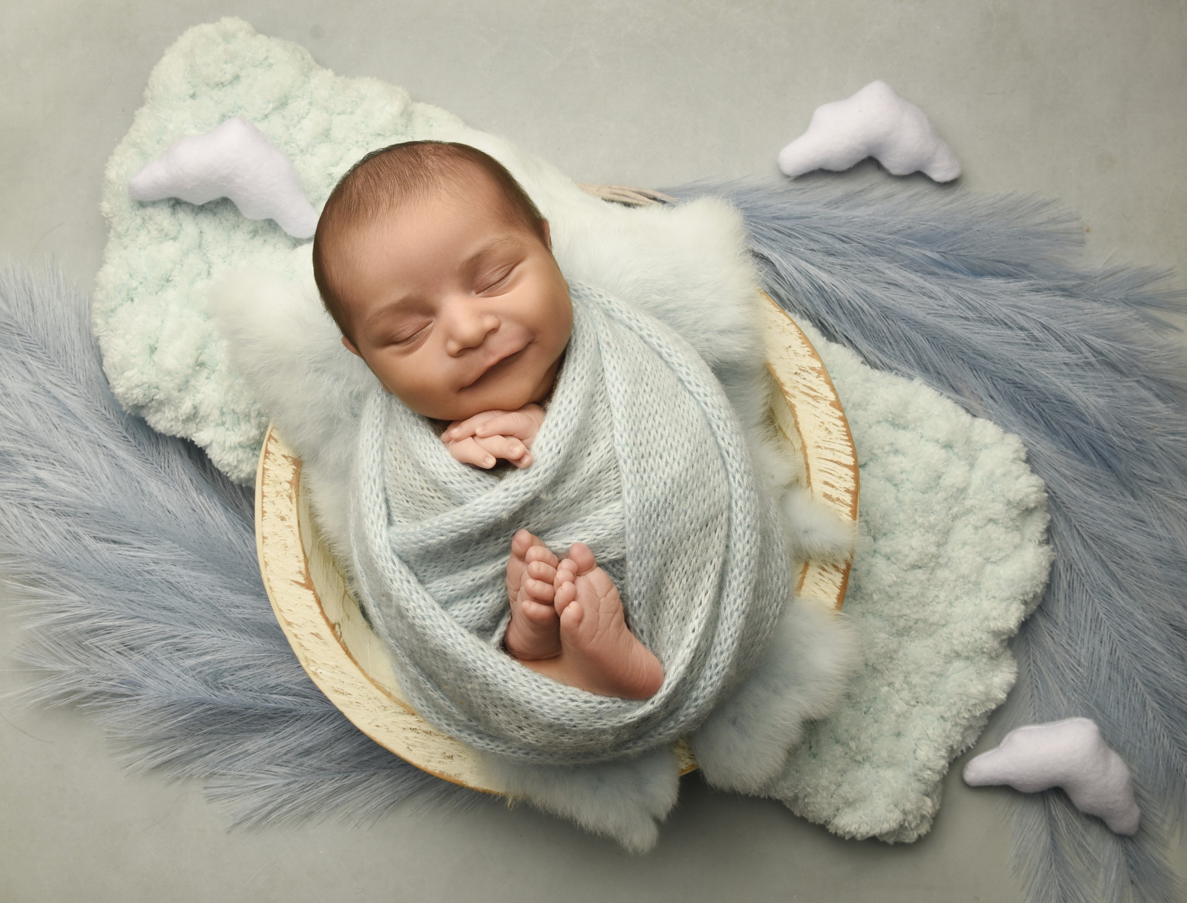 Smiling newborn wrapped in pale blue with cloud props